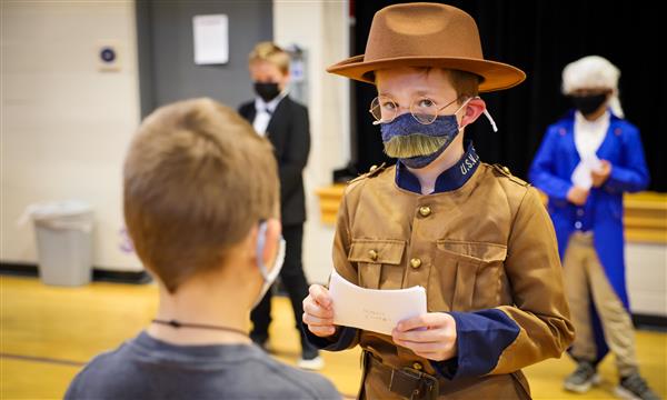 A boy dressed as Teddy Roosevelt speaks to younger students
